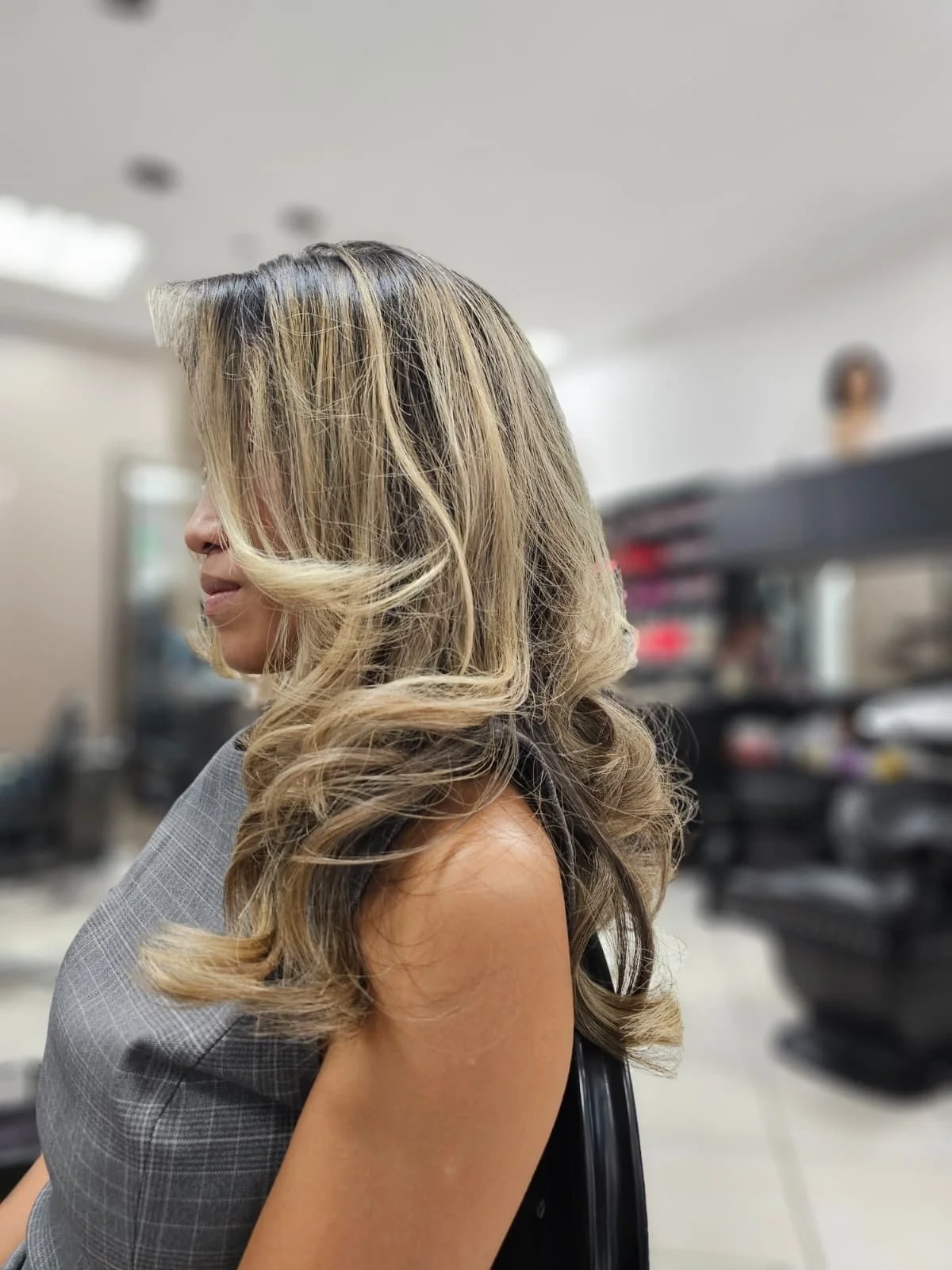 Woman with shoulder-length, styled blonde hair sitting in a salon chair, blurred salon background.