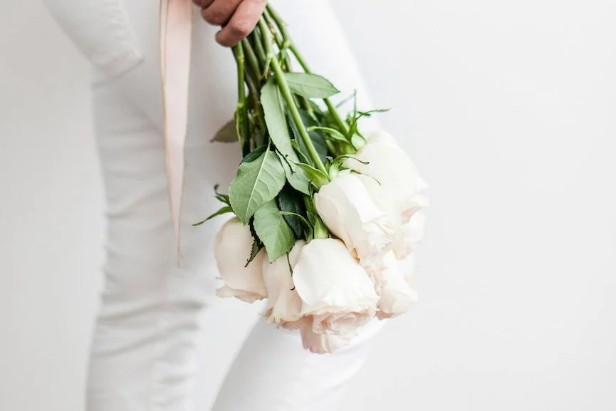 A woman in white holding a bouquet of white roses at her side, a quiet moment before a date.