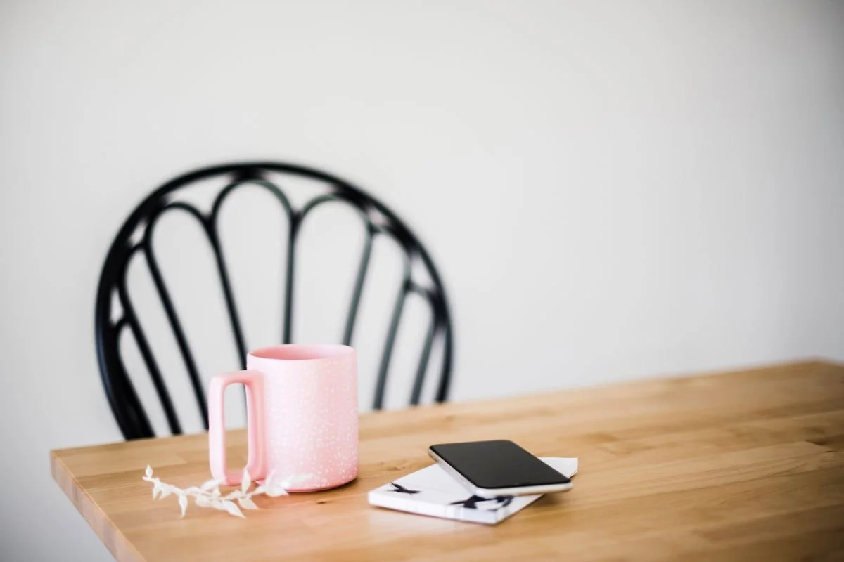 A pink mug and a phone resting on a wooden table beside a black chair, a quiet spot set aside for a morning routine.Terri Cole quote graphic: "Your job as a grown up is to set the boundaries that work for you in your adult life."