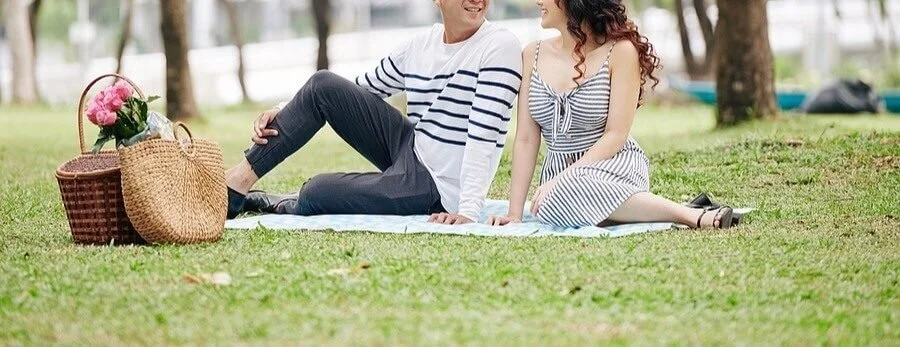 A couple sitting close together on a picnic blanket in a park, enjoying a relaxed, low-pressure date.