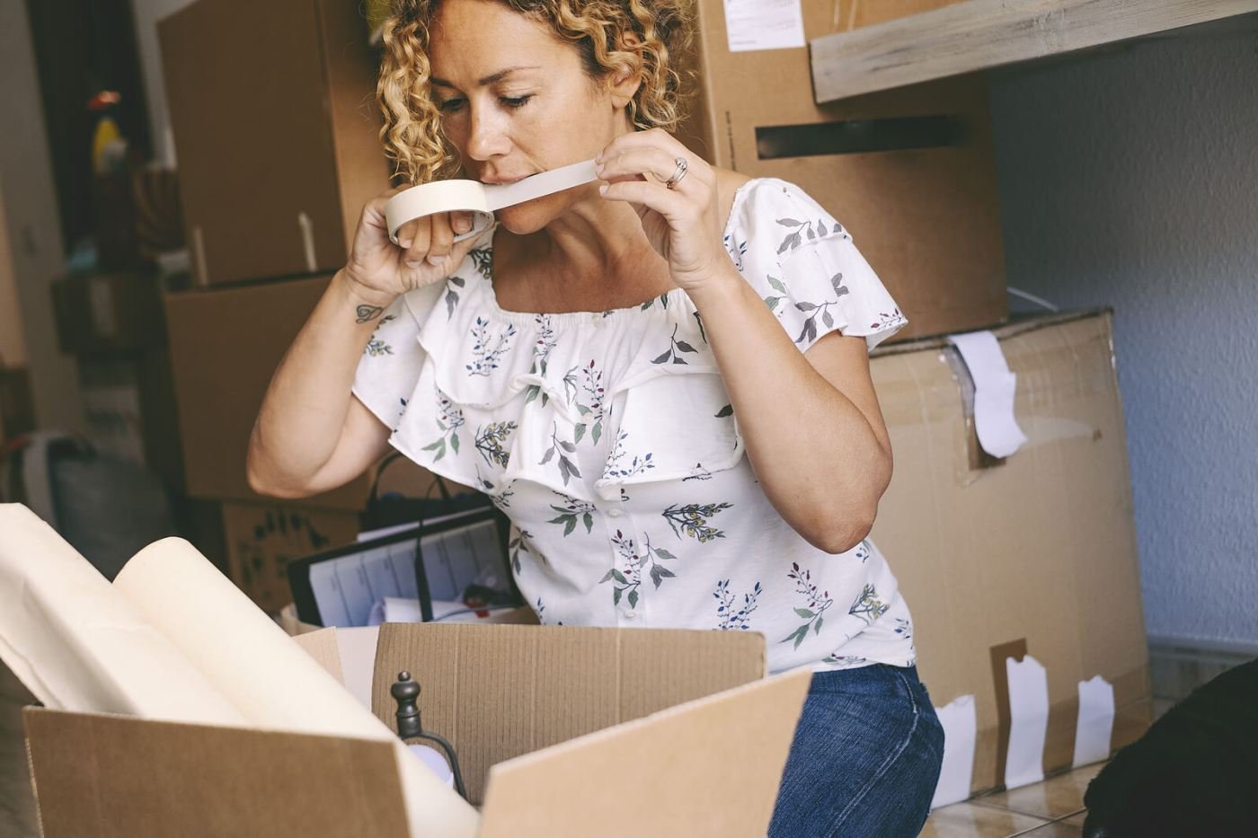 A woman with curly hair standing among cardboard boxes in the middle of packing, one of the many small tasks of a move.