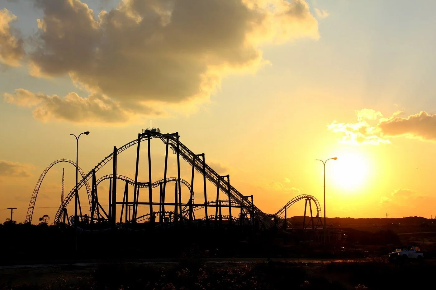 A roller coaster silhouetted against an orange sunset sky, a reminder of the thrills and the sensory load of a theme park.