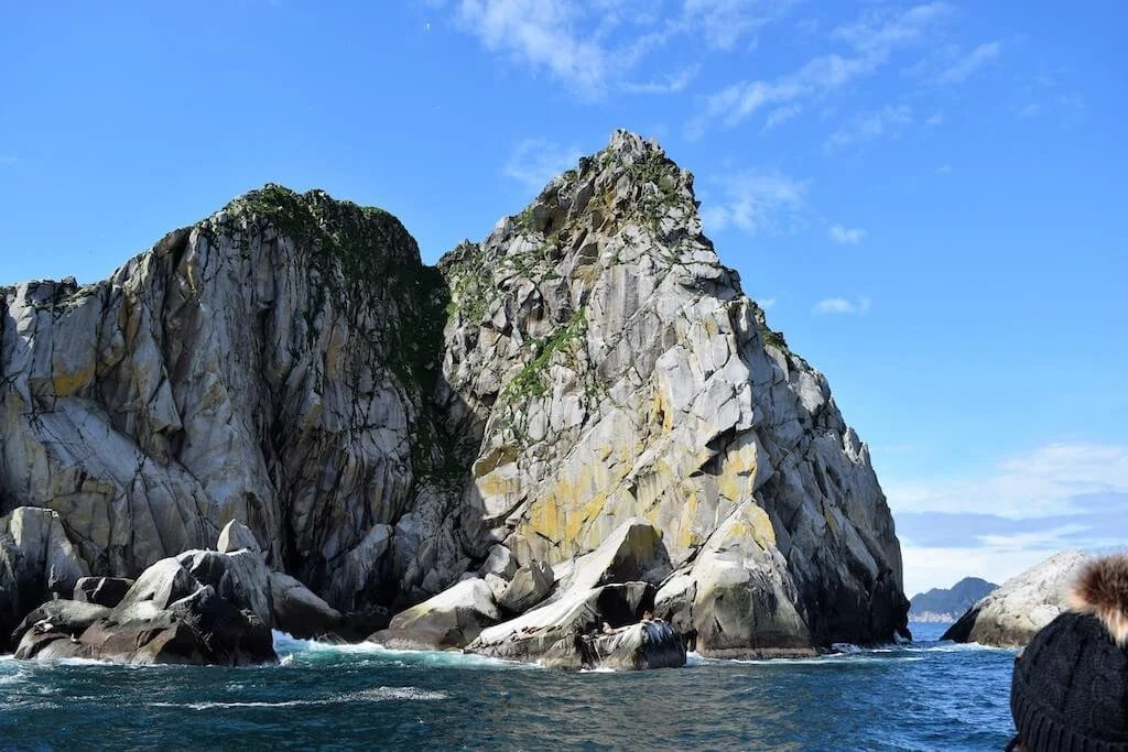 A rocky outcrop rising from blue water in the Kenai Fjords in Alaska, for introverts planning a trip.