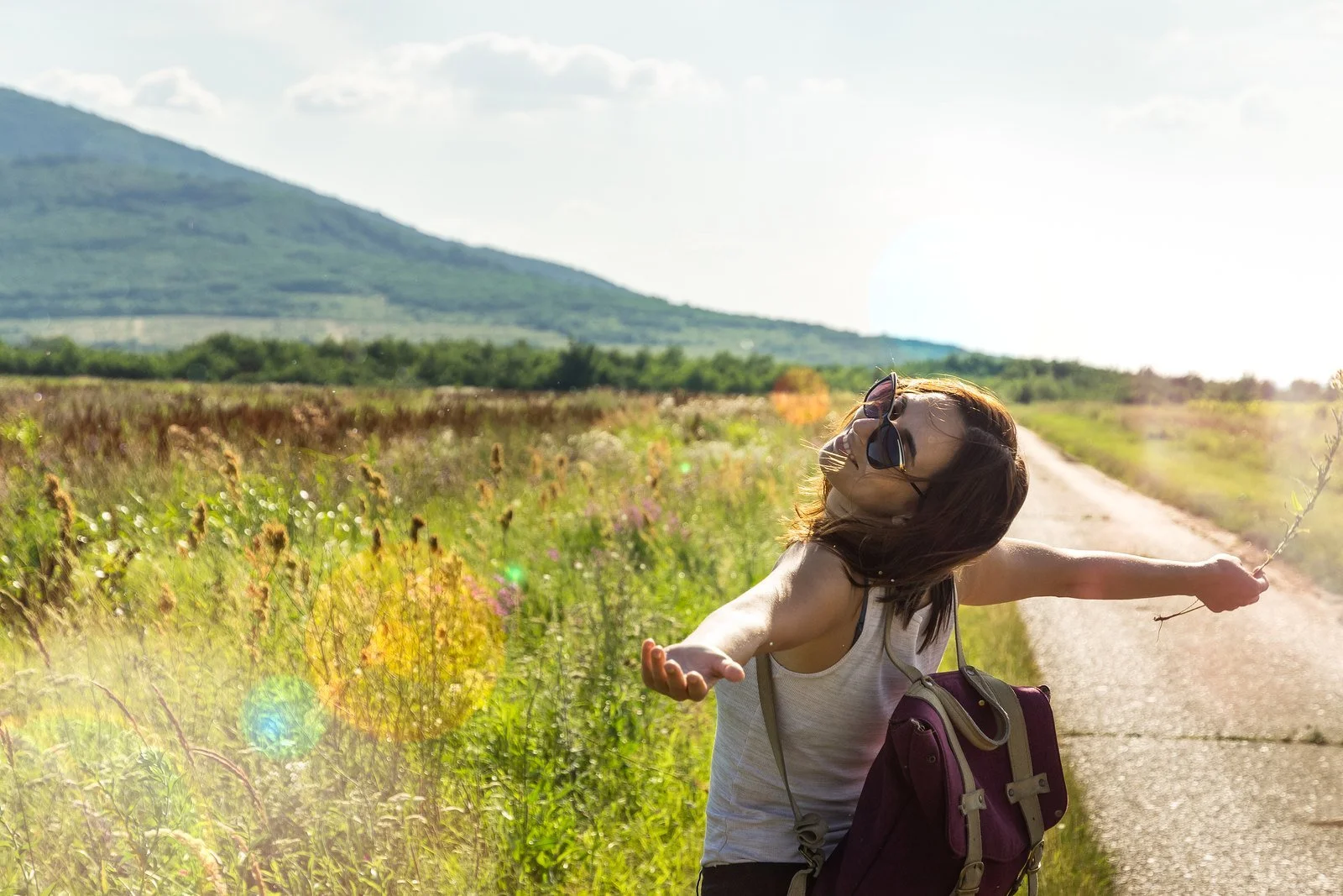 A woman standing in a sunny field with her arms open wide, feeling free and confident.