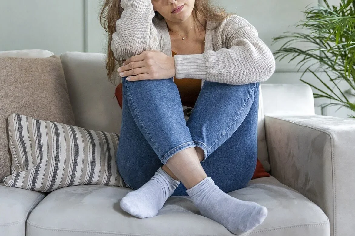 A woman sitting on a couch hugging her knees in cozy socks, taking a quiet break from the news.