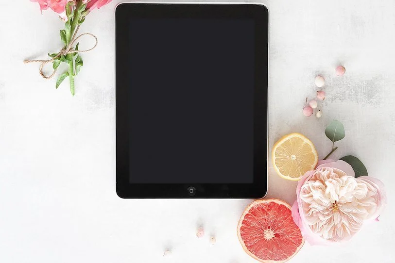 A tablet resting beside pink flowers and citrus on a white table, a calm setting for thinking through online dating.