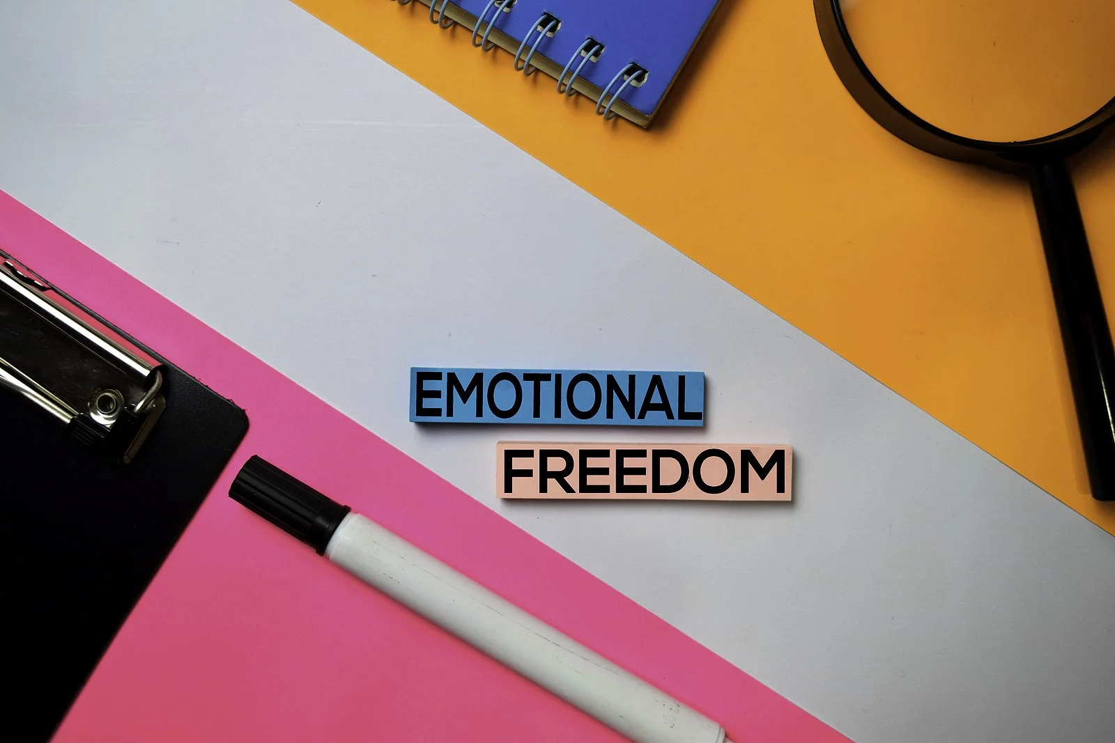 The words Emotional Freedom on a desk beside a pen, a clipboard, and a magnifying glass.