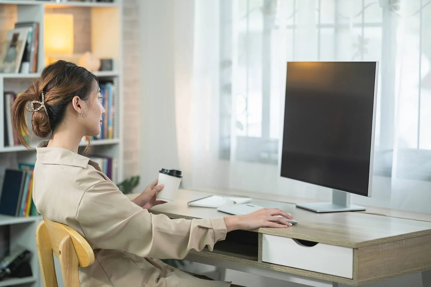 A woman sitting at a desk working on a computer in a bright home office, thinking through a big decision.