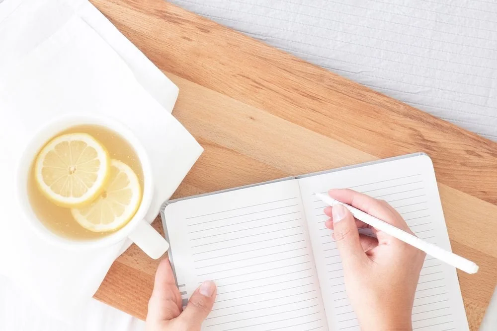 A woman’s hands writing in an open journal beside a cup of lemon tea.Boundary script graphic: Acknowledge, set the Boundary, then offer a Creative Yes when a parent criticizes your choices.