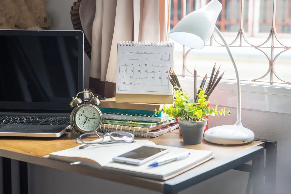 A tidy desk with a laptop, a desk calendar, an alarm clock, glasses, and a notebook, a quiet space set up for an online therapy seBoundary script graphic: Acknowledge, set the Boundary, then offer a Creative Yes when a parent criticizes your choices.