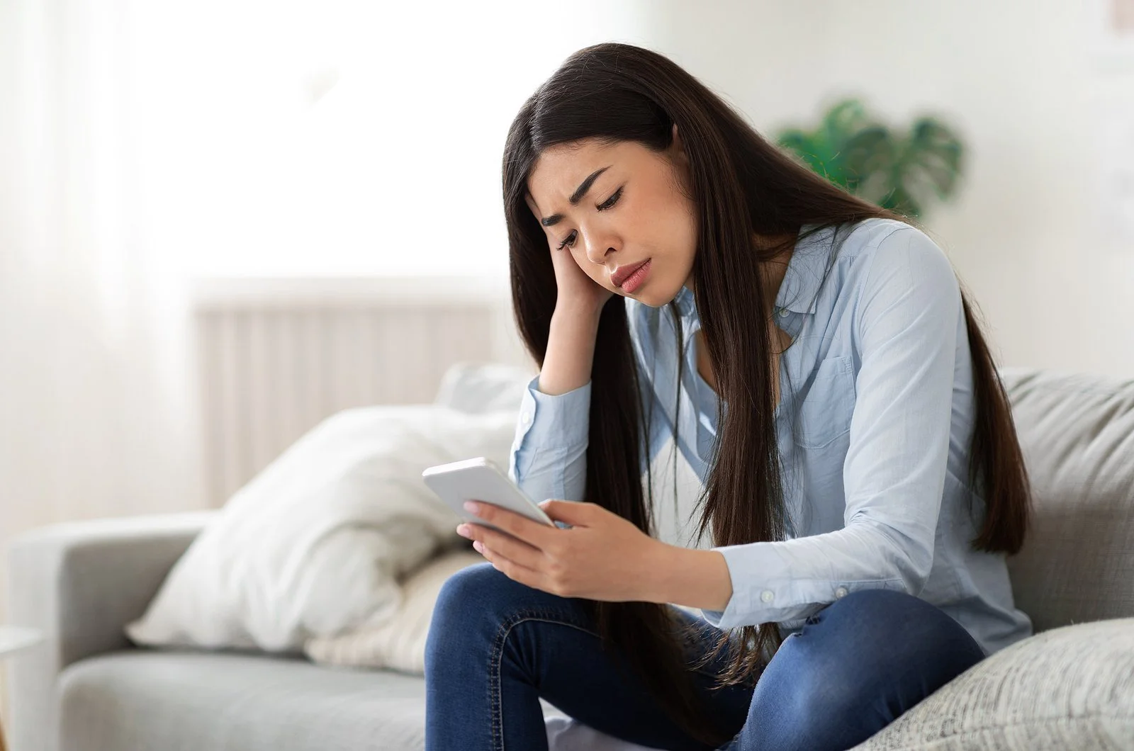 A woman sitting on a couch looking worried while she checks her phone, a common moment for women with codependent patterns.