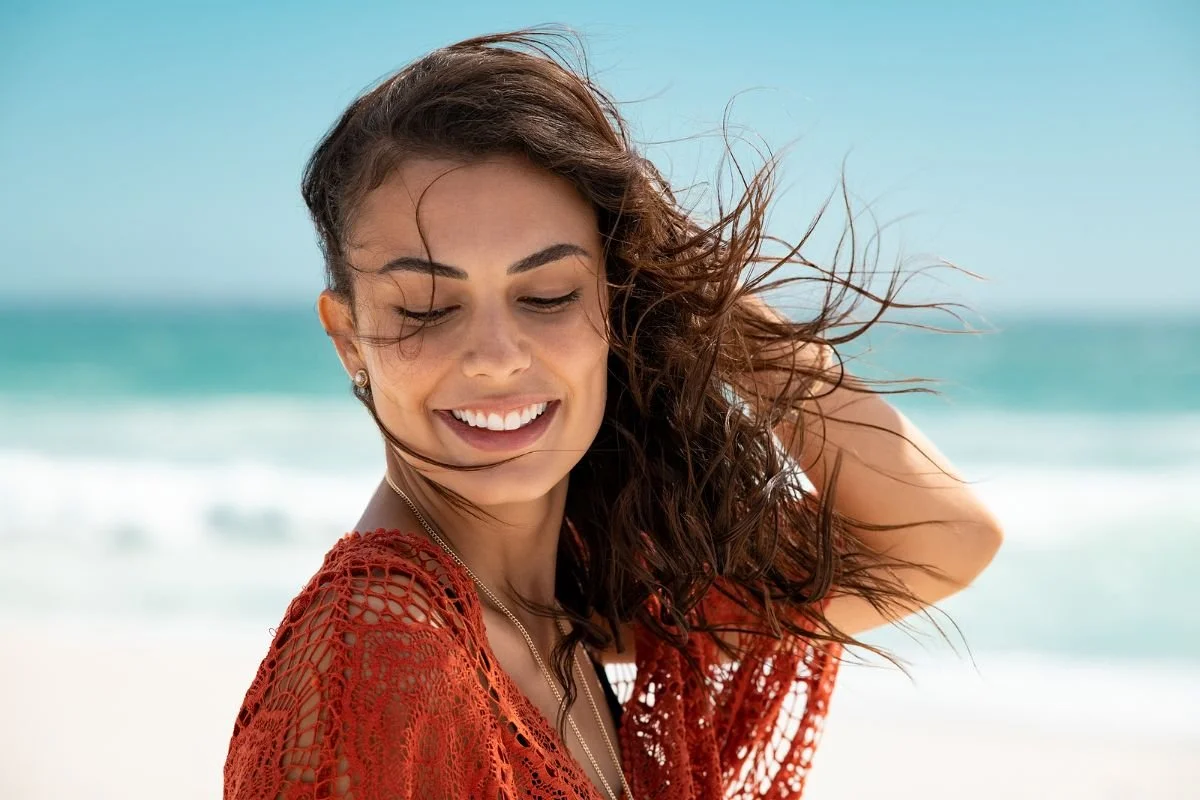 A woman smiling on a sunny beach with her hair blowing in the wind, feeling lighter.Boundary script graphic: Acknowledge, set the Boundary, then offer a Creative Yes when a parent criticizes your choices.