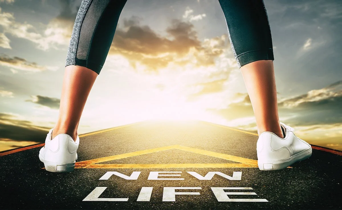A woman standing on a road at sunset with the words new life painted at her feet, ready for what comes after divorce.