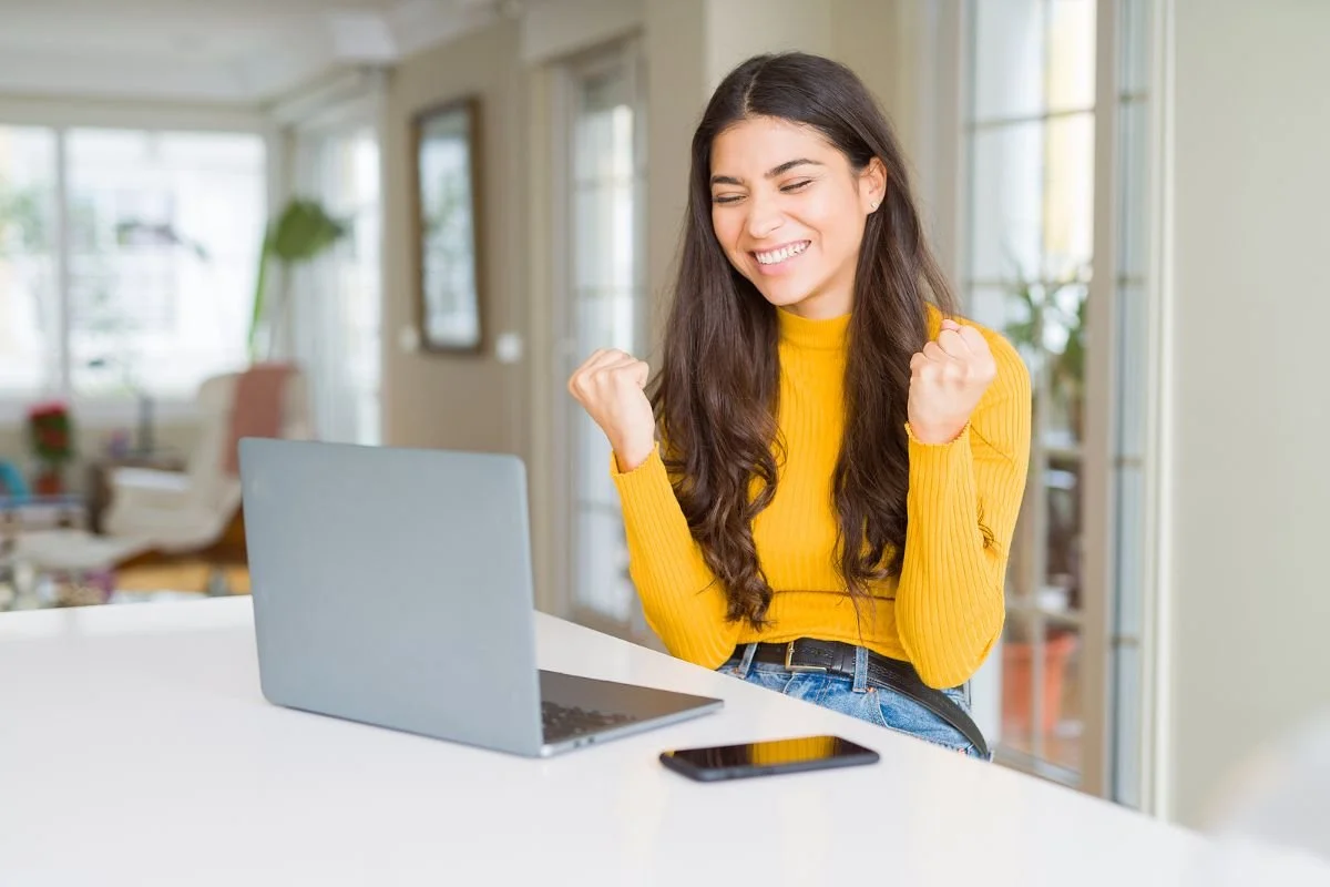 A smiling woman in a yellow sweater at a laptop in a bright room, pleased with how her online session is going.Terri Cole quote graphic: "Your job as a grown up is to set the boundaries that work for you in your adult life."