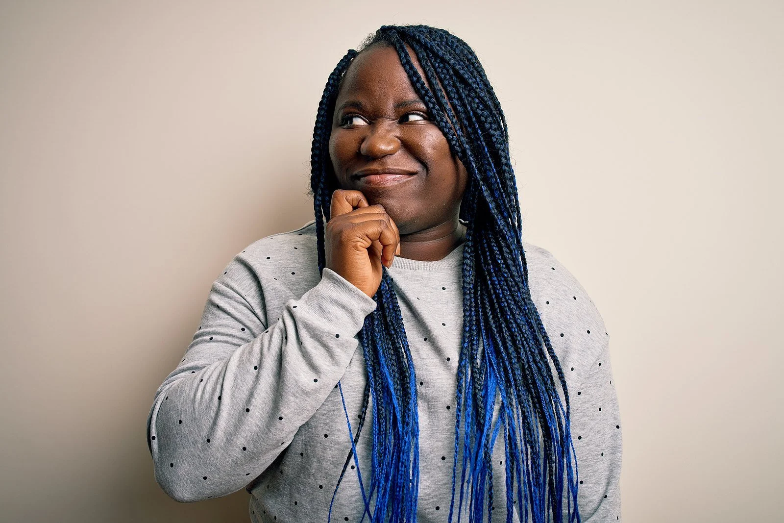 A woman with braids resting her hand on her chin as she reflects on the signs of self-sabotage in her own life.