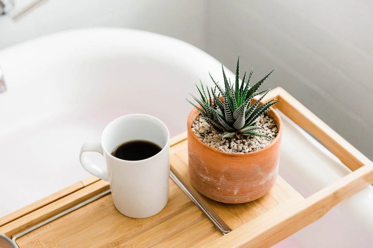 A wooden tray across a bathtub holding a cup of coffee and a small plant, a quiet space that protects personal time.
