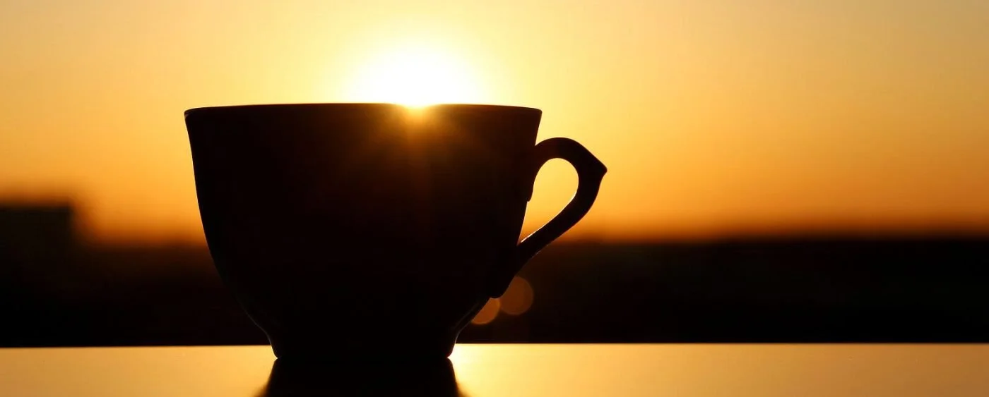A cup of coffee silhouetted at sunset, a quiet summer self-care ritual.