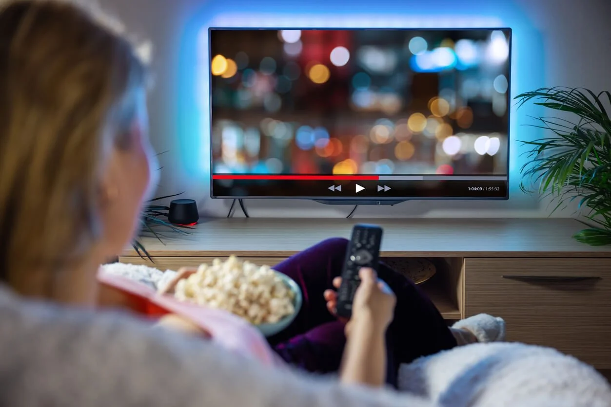 A woman holding a bowl of popcorn while watching a movie at home, choosing entertainment she enjoys.
