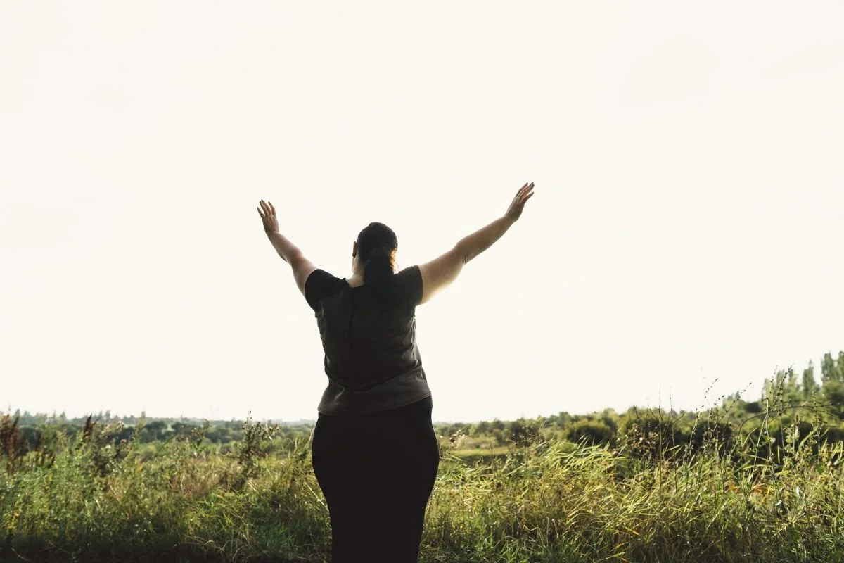 A woman seen from behind with her arms raised in an open grassy field, feeling free and fulfilled.Boundary script graphic: Acknowledge, set the Boundary, then offer a Creative Yes when a parent criticizes your choices.