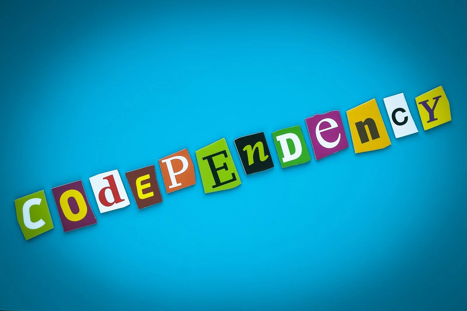 The word codependency spelled out in colorful cut-out letters on a bright blue background.