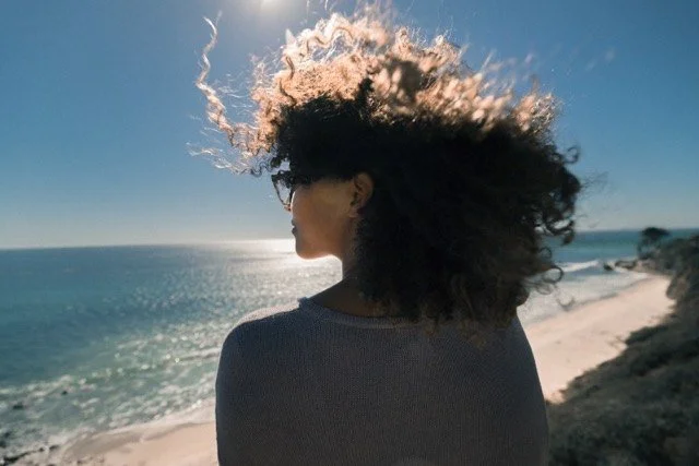A woman with curly hair looking out over a sunny Florida beach, a peaceful place to take an online therapy session.