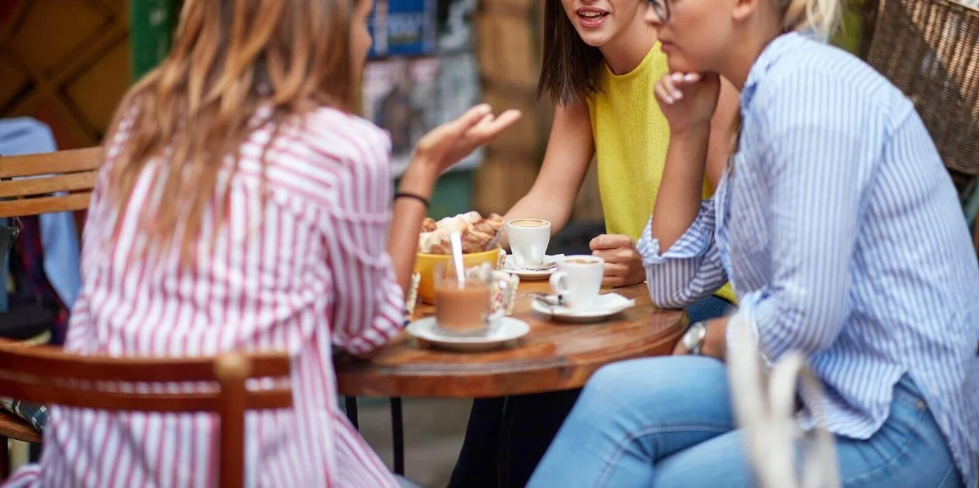 Three women talking over coffee and pastries at a cafe table, a reminder that talking with someone who understands helps during sudden change