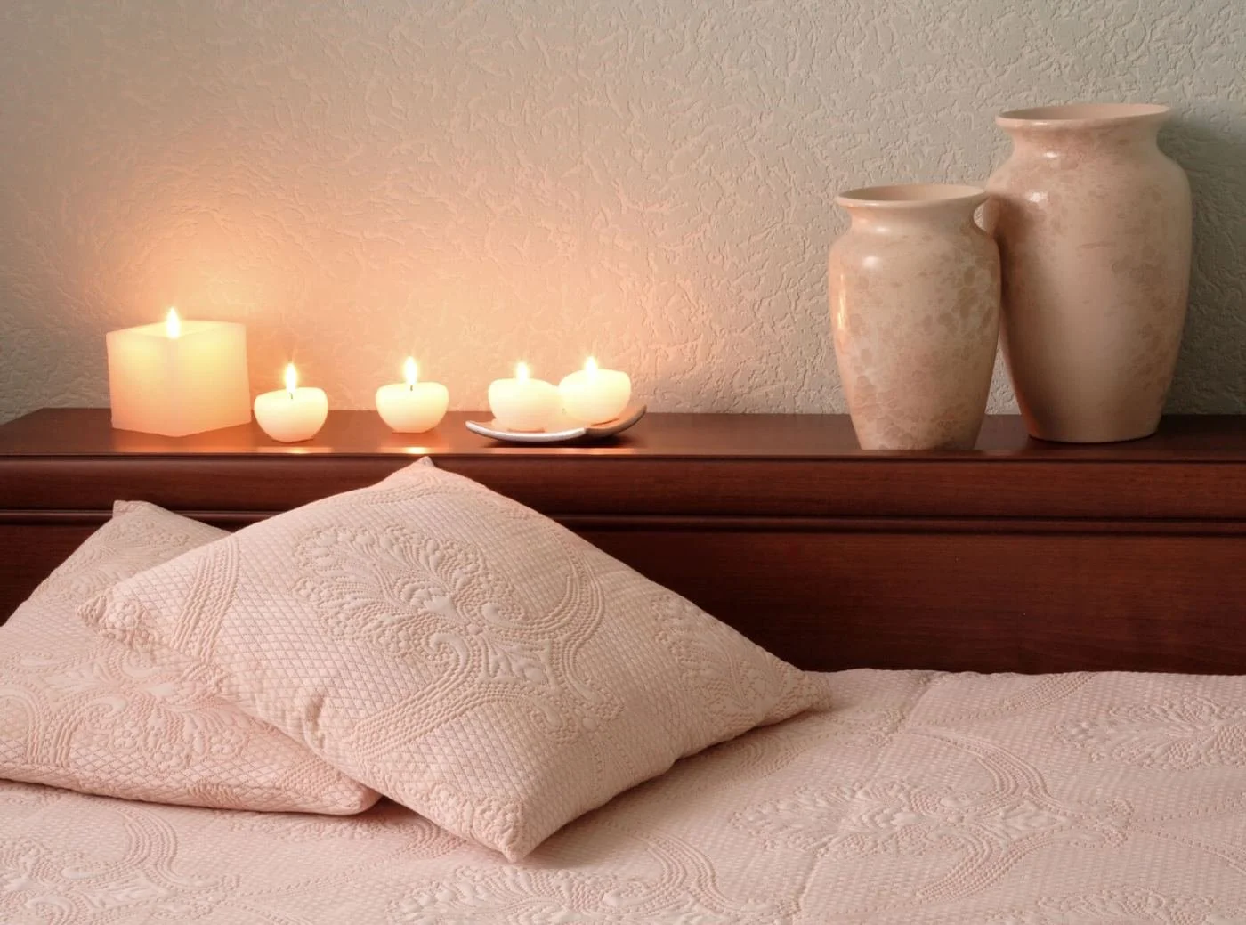 Lit candles near a bed in a softly lit bedroom, a calm setting that can help a sensitive woman relax.