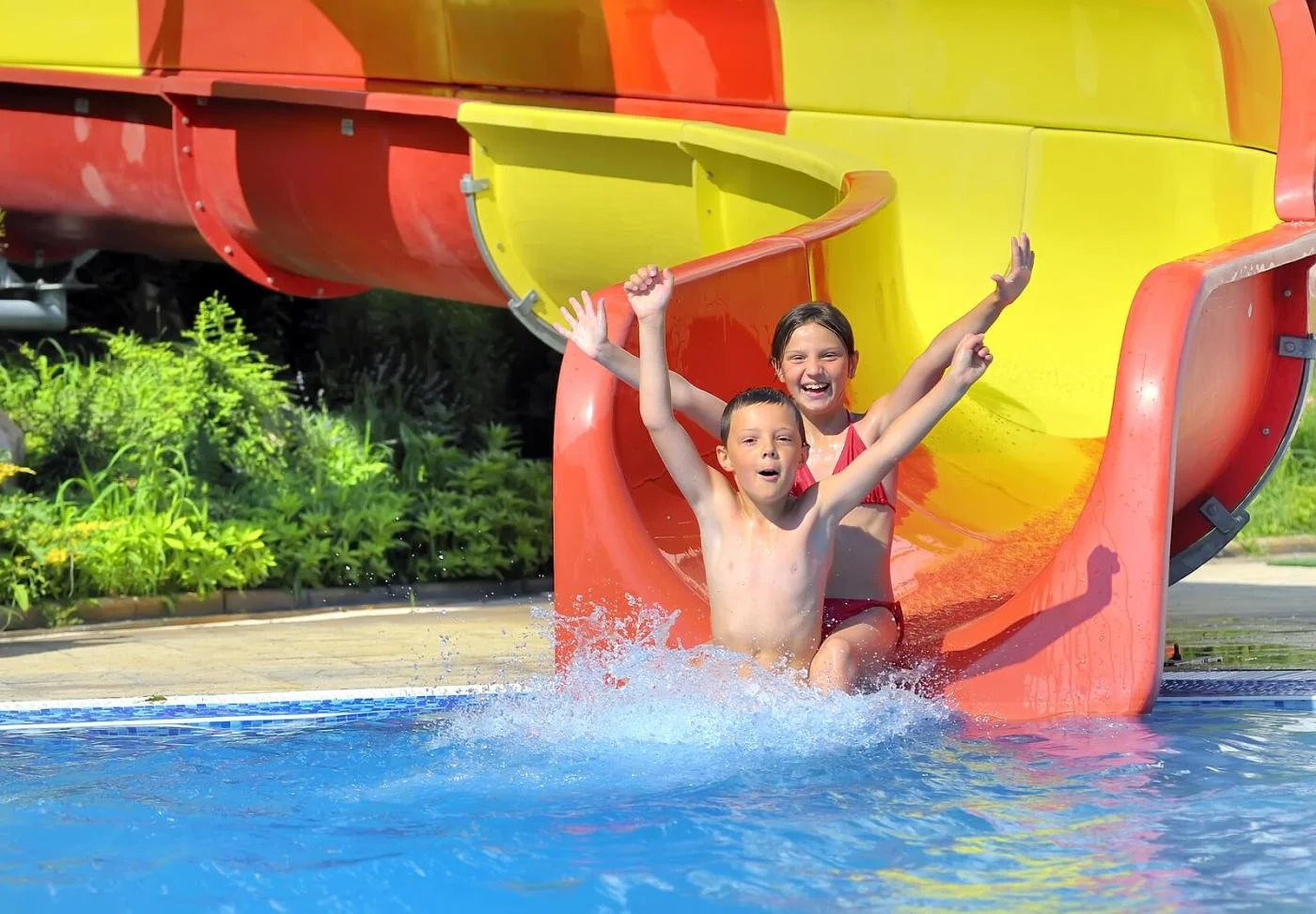 A child sliding down a bright red and yellow water slide into a pool, capturing the splash and noise of a theme park day.