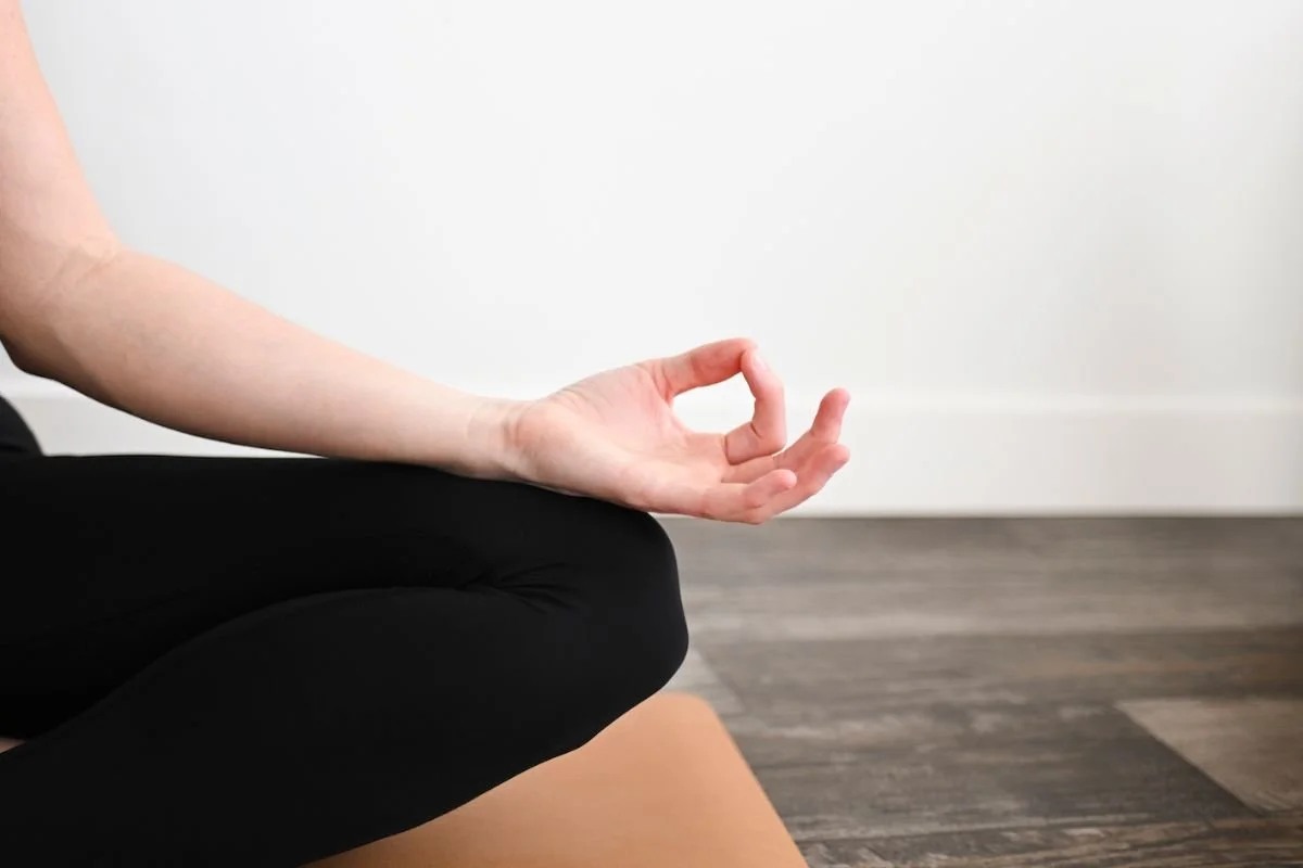 A woman seated in a meditation pose with her hand in a gentle mudra, taking a few minutes to reset in the afternoon.