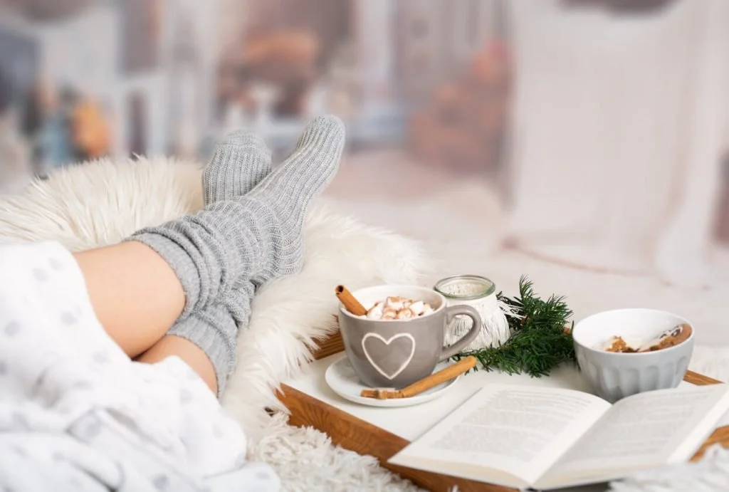 Feet in warm socks propped on a table next to a mug of cocoa and an open book, a picture of an introvert recharging.