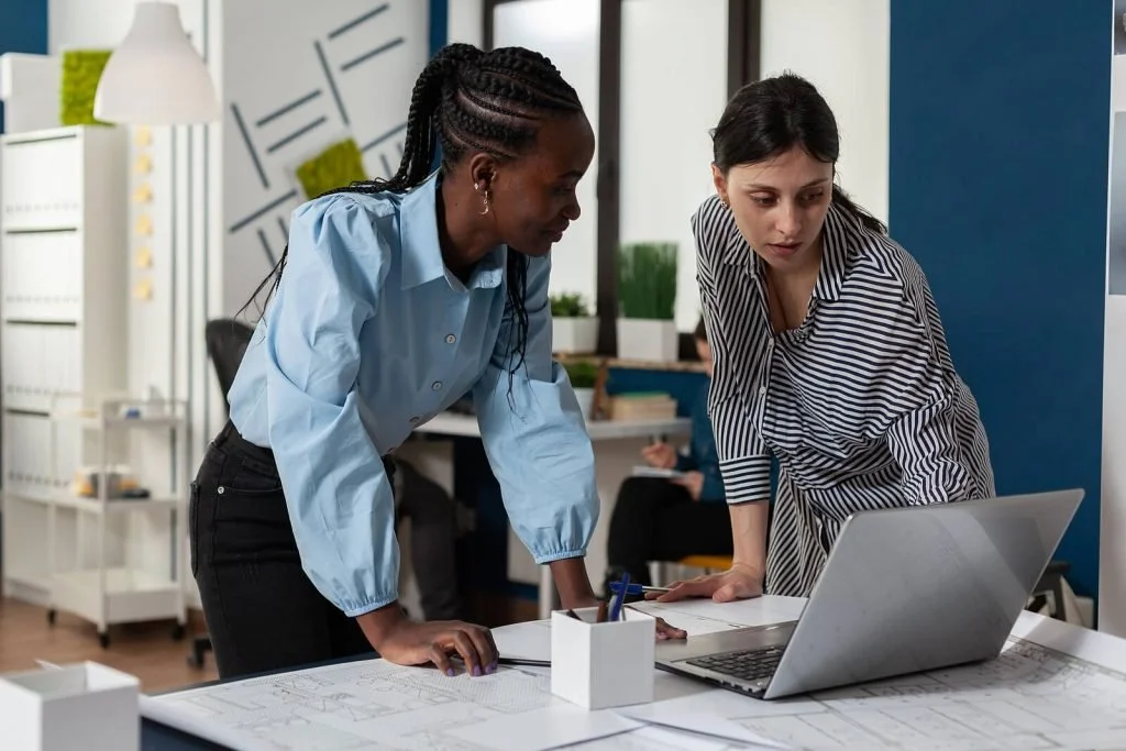 Two women working together around a laptop in a calm office.