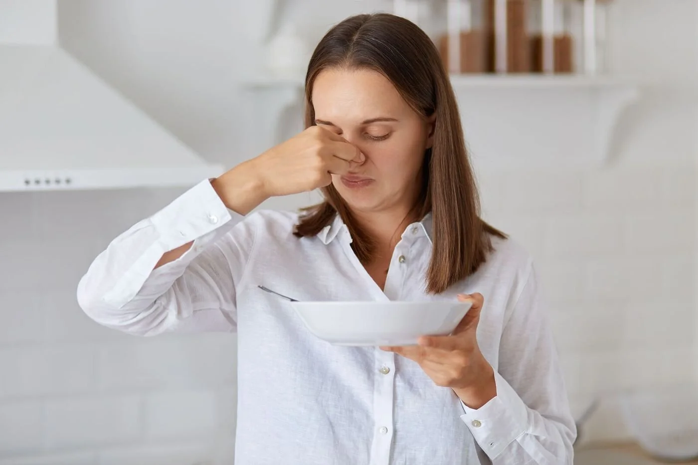 A woman reacting to the smell of food she dislikes, for a highly sensitive person navigating mealtimes.