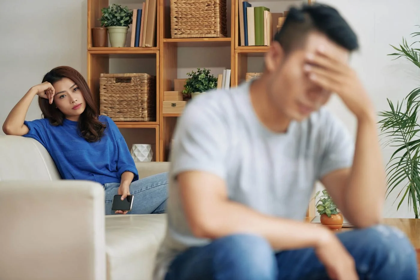 A woman and a man on a couch looking worried, one resting her head on her hand and the other holding his forehead, showing tension in a relationship.