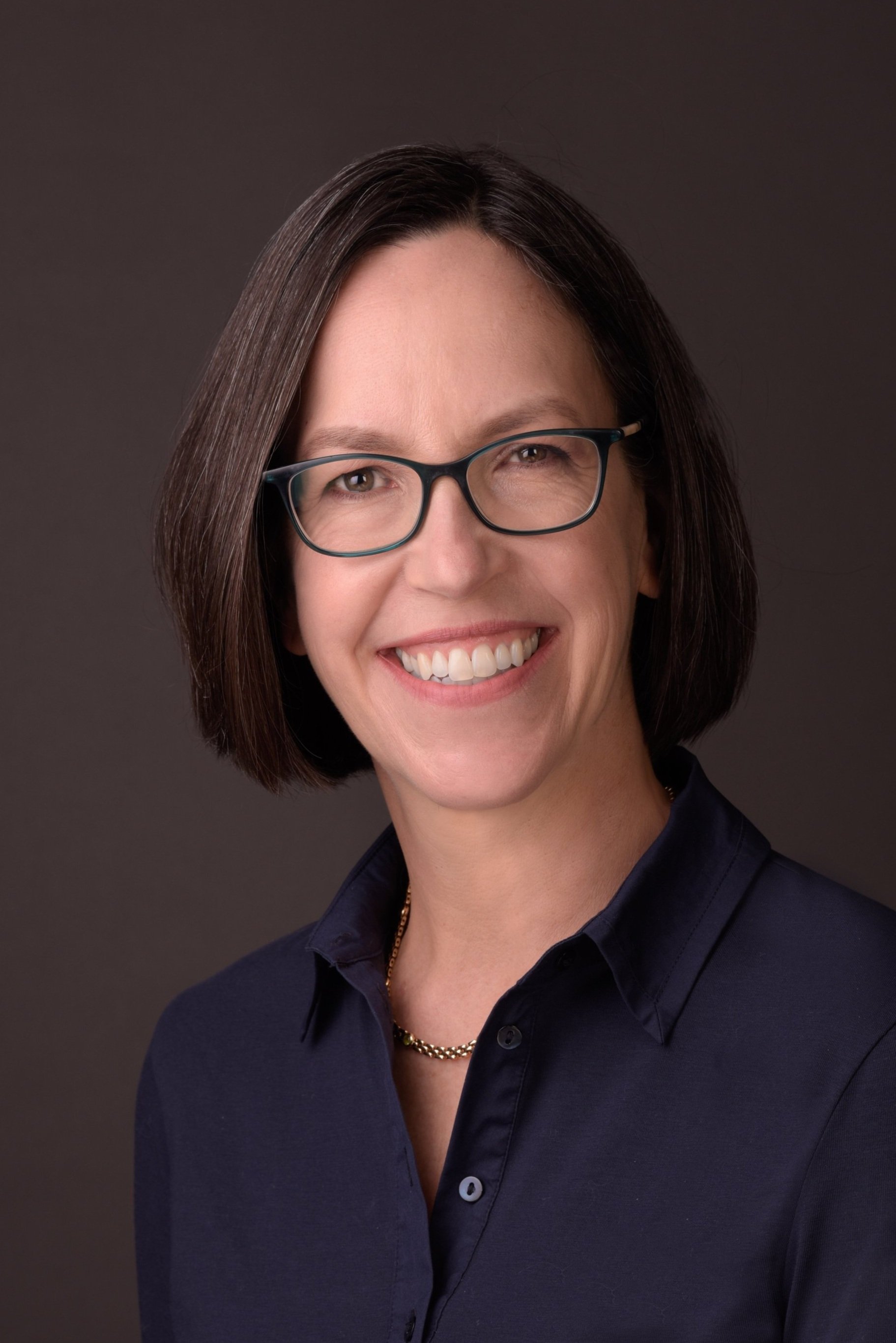 A headshot of Jacqui Robbins, a 50-something white woman with brown hair, glasses, and a big smile.