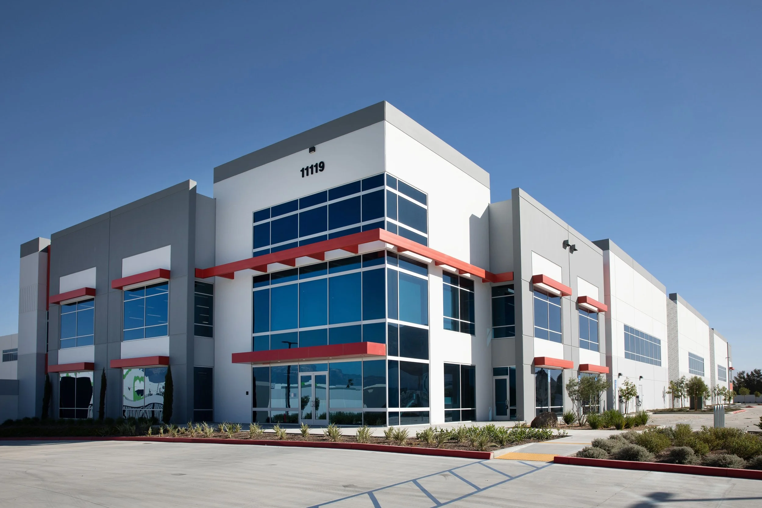 Modern commercial building with large glass windows and white exterior, numbered 11119, under a clear blue sky.