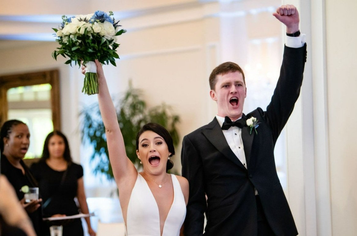 Bride and groom celebrating at their wedding, with the bride holding a bouquet up and both raising their fists in victory