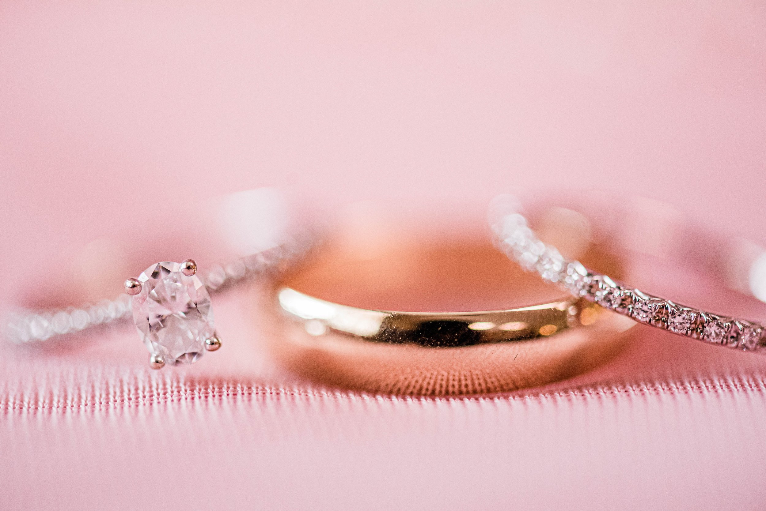 Close-up of three rings on a pink satin background, including a plain gold band and a diamond-studded band.