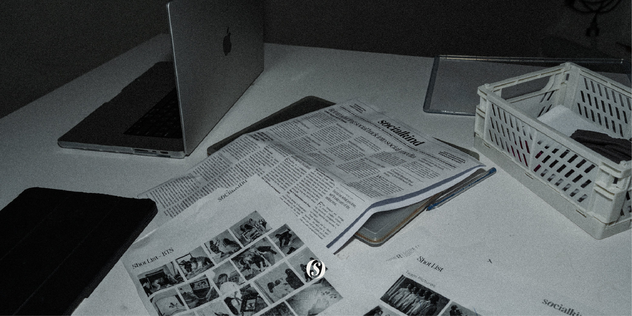 a busy desk scattered with newspaper, prints, laptops and plastic crates