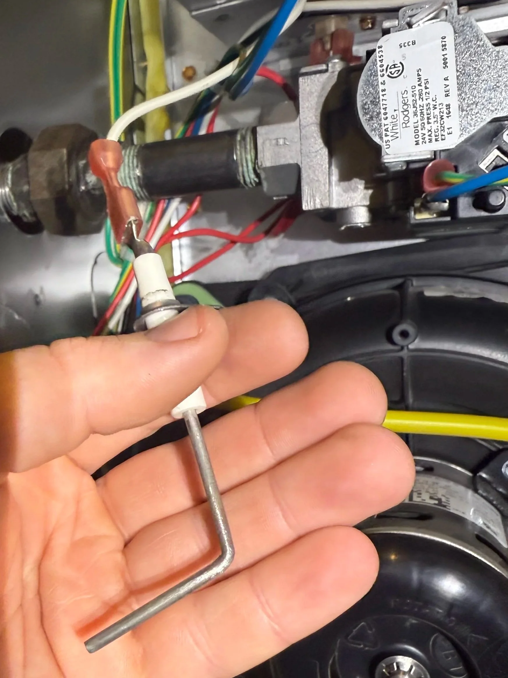 Close-up of a person's hand holding a flame sensor, inside a furnace