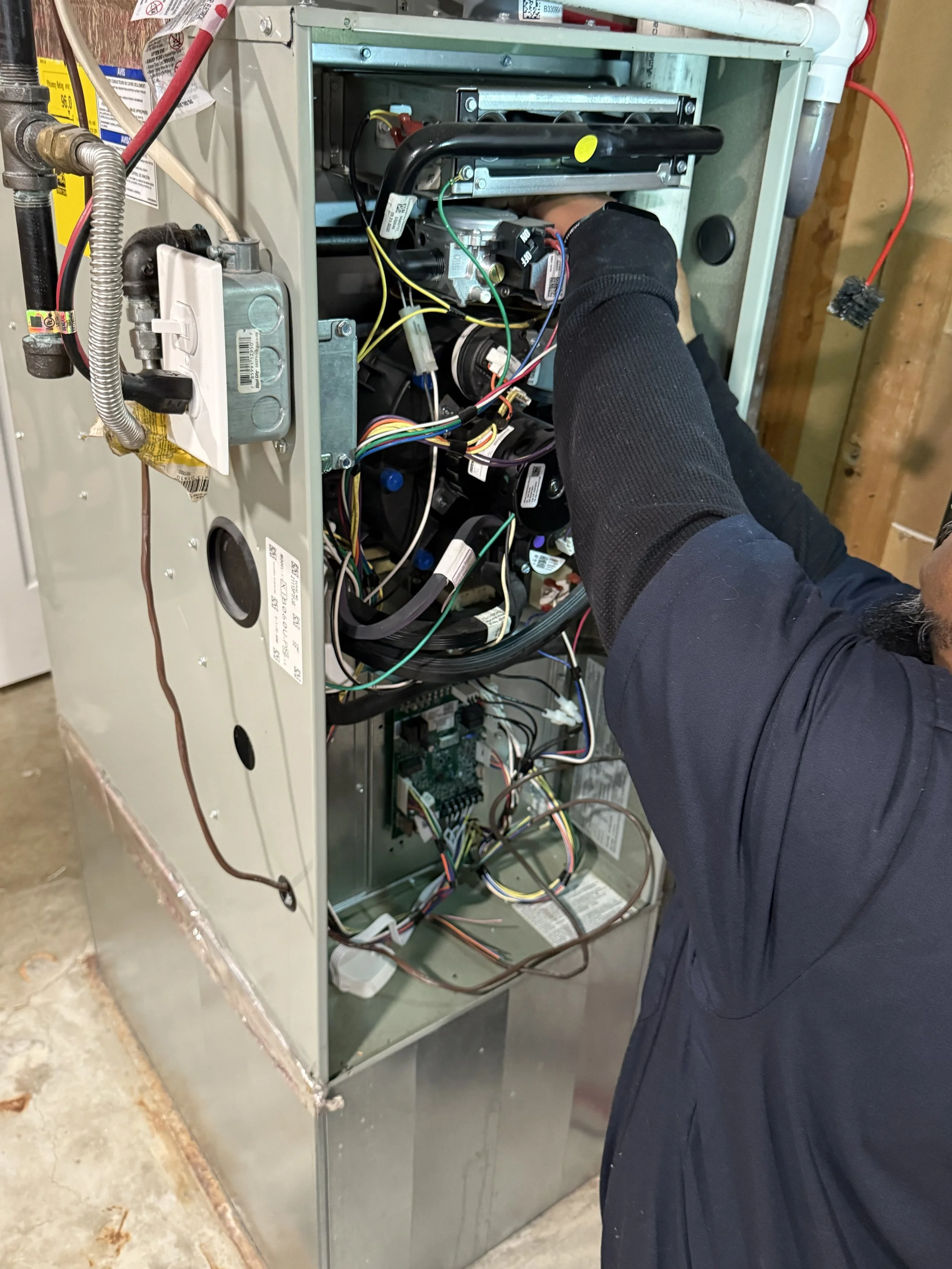 Technician repairing or inspecting the internal components of an HVAC or furnace unit, with various wires and parts visible inside the metal casing.