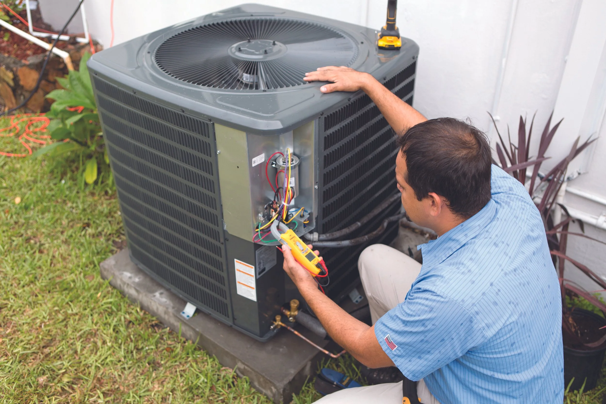 A technician inspecting and testing an outdoor air conditioning unit with a digital multimeter.