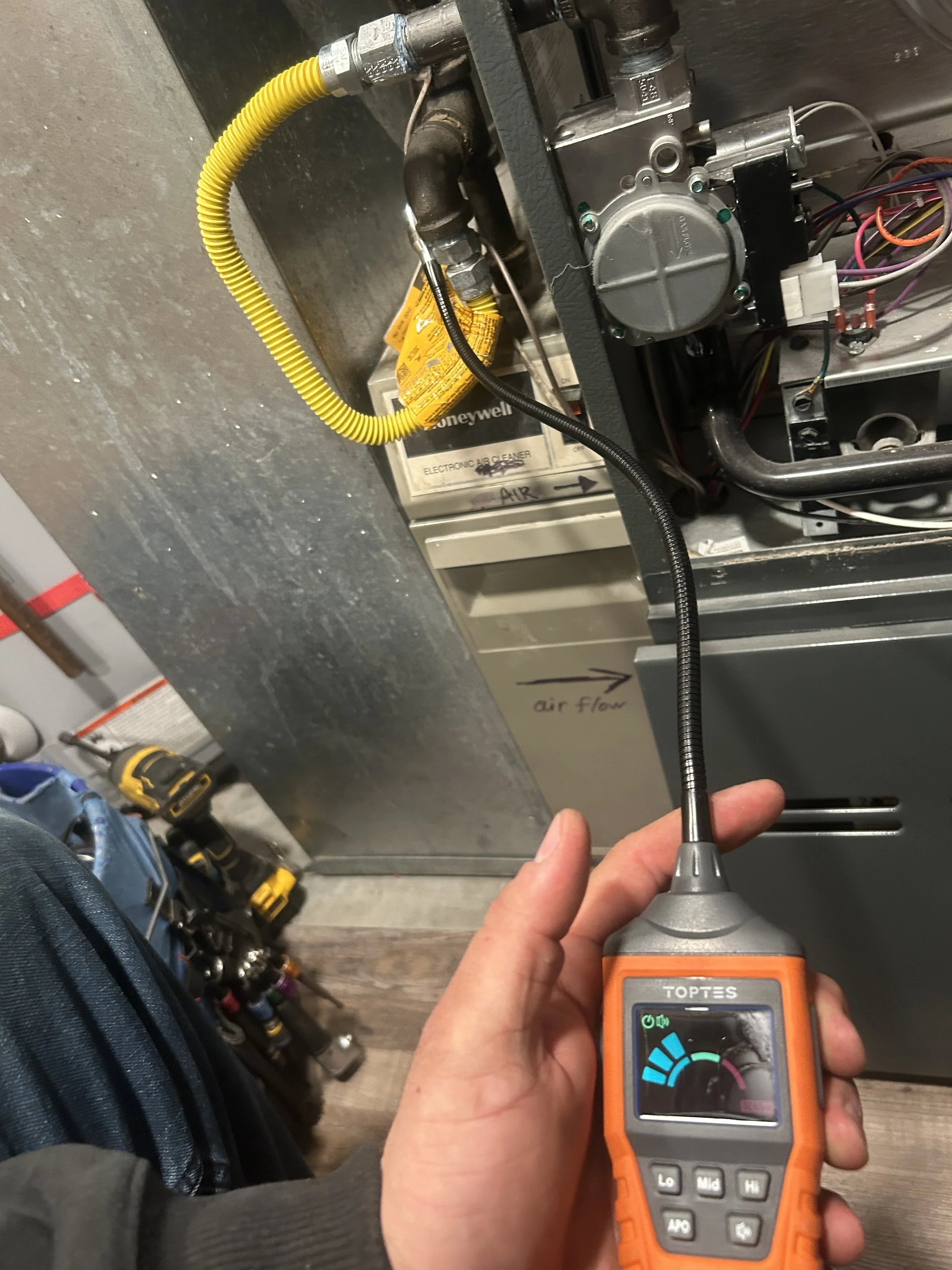 Technician testing electrical components of an HVAC unit using a digital multimeter or tester, with an air flow diagram and tools nearby.