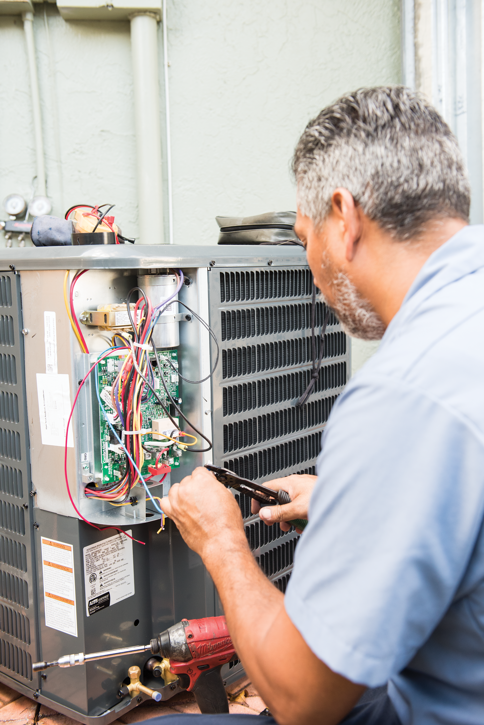 Man repairing an air conditioning unit with a screwdriver.
