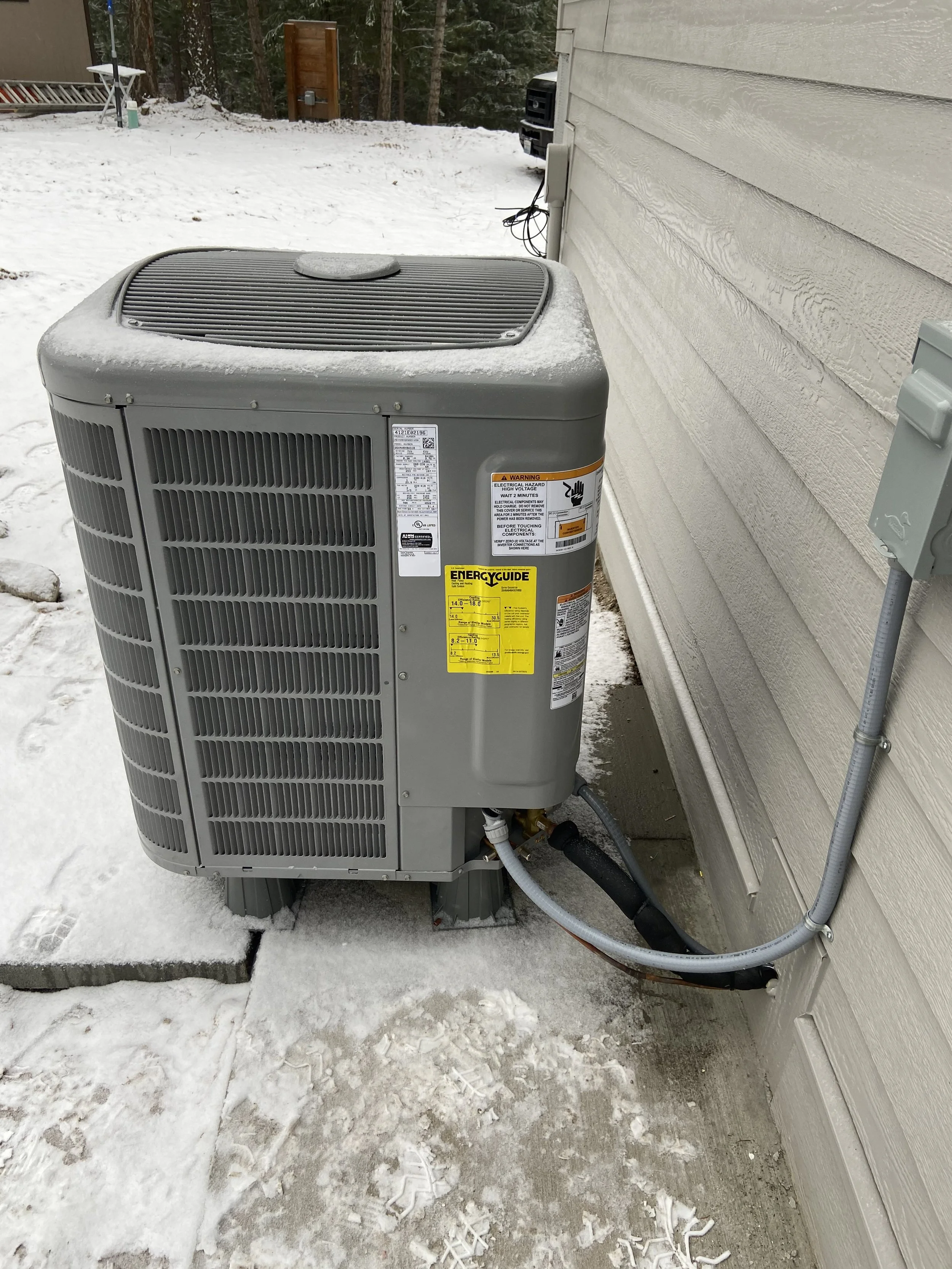 An outdoor air conditioning unit installed beside a house with snowy ground and some footprints.