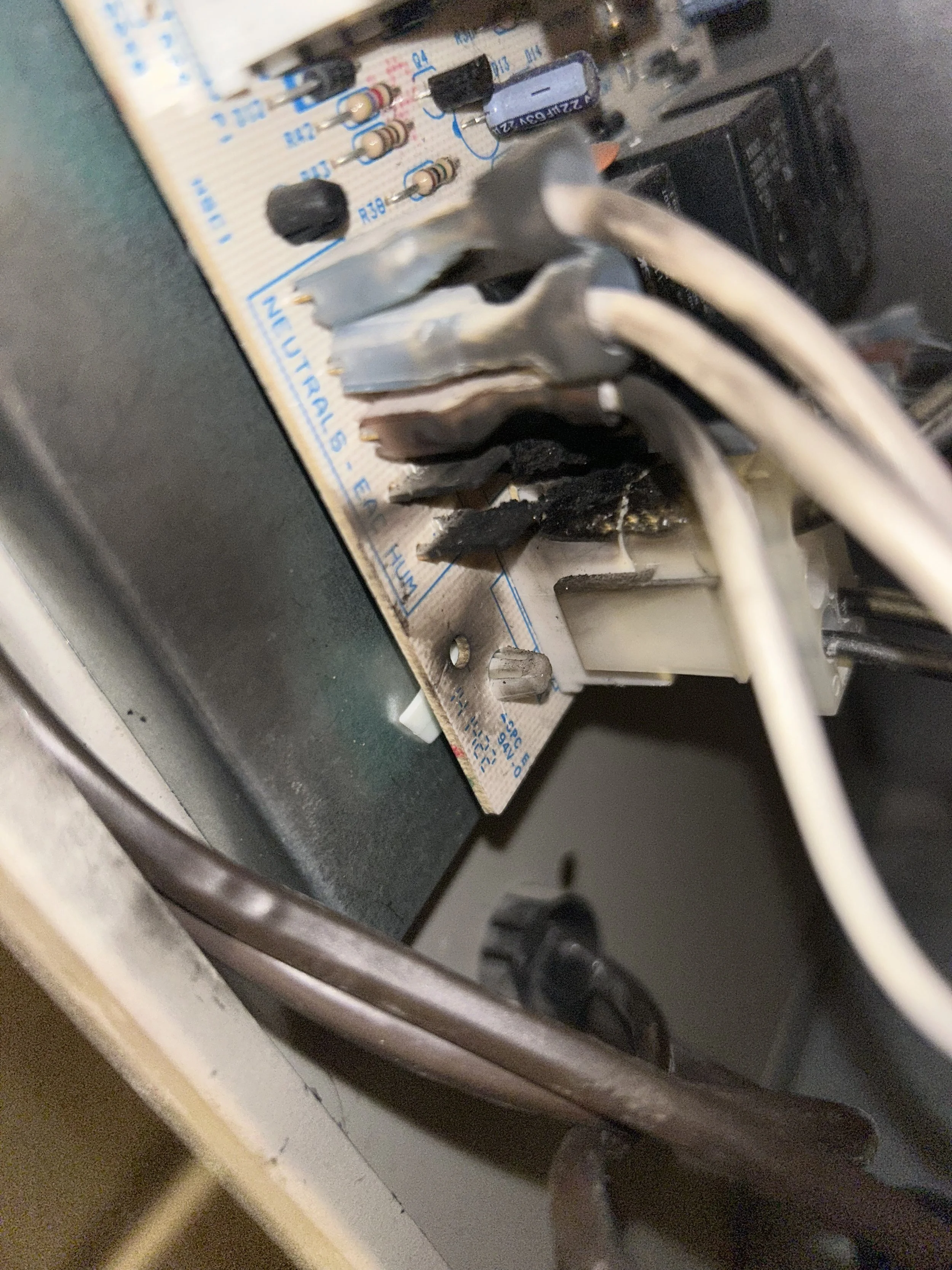 Close-up of an electronic circuit board with wiring and components attached, showing some blackened areas indicating potential damage or burnt components.