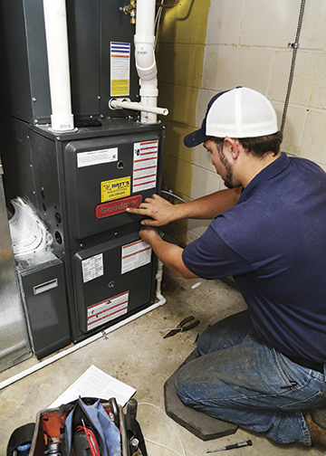 Technician working on a furnace or HVAC system in a basement or utility room.