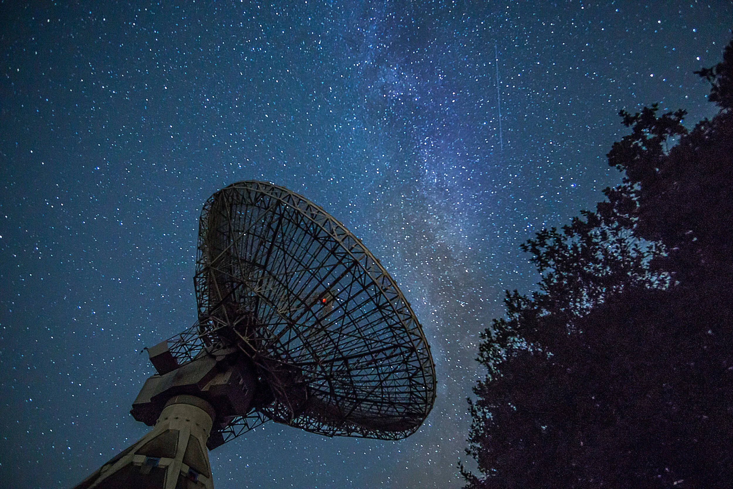 Radio telescope dish against a starry night sky with Milky Way visible.