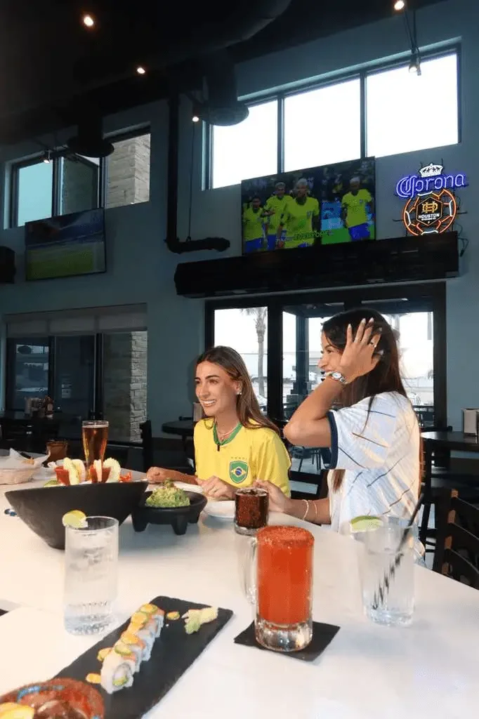 Guests enjoying seafood and drinks while watching a soccer match at El Muelle Seafood in Houston.