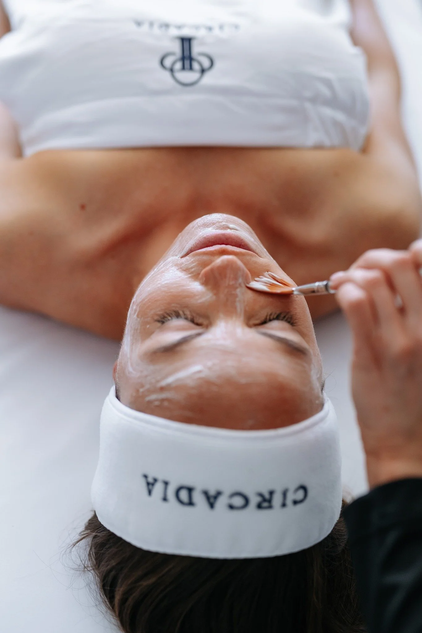 Woman getting lotion brushed on face during facial