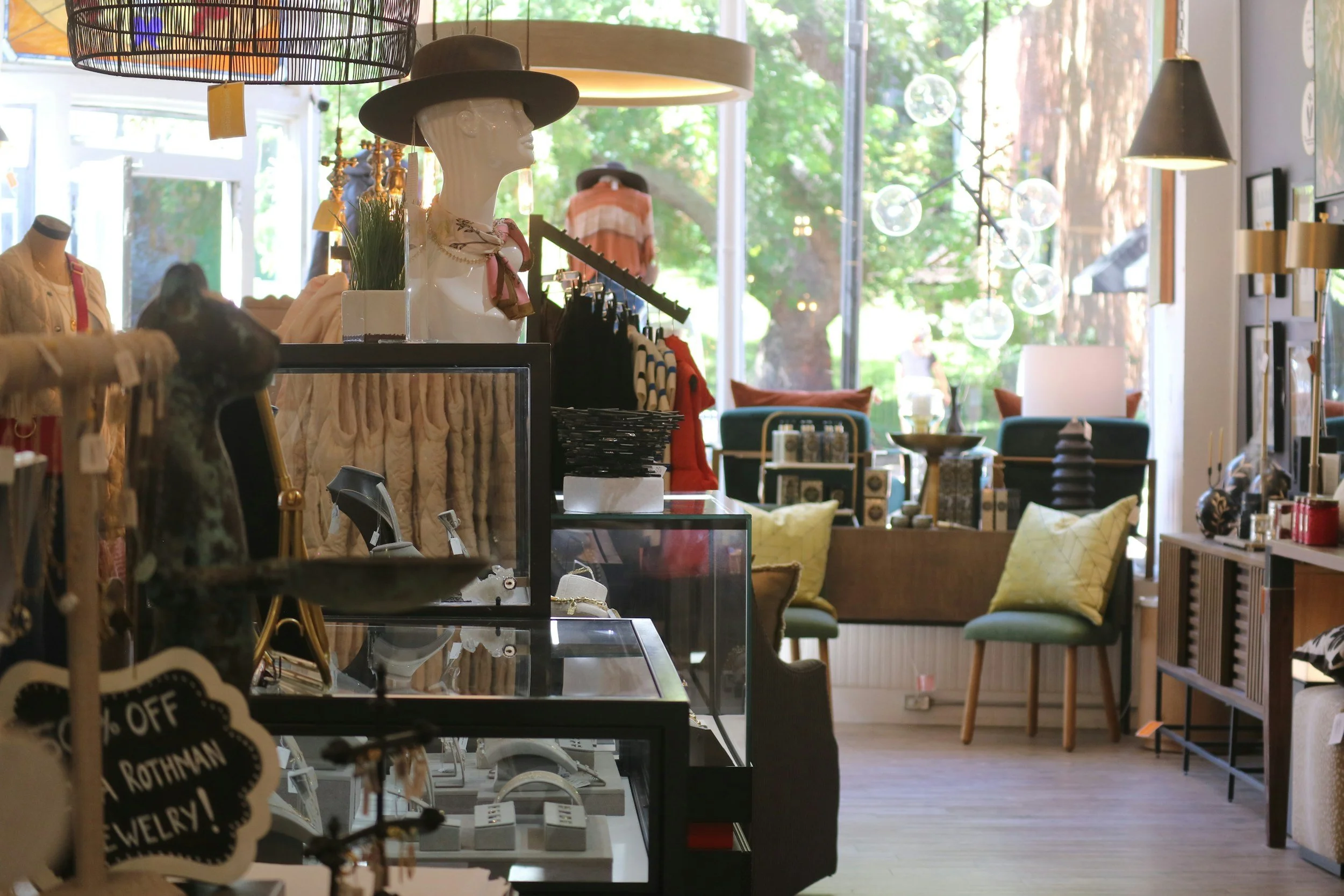 Boutique setting with hanging clothing, jewelry displays, furniture and mannequin head wearing a hat